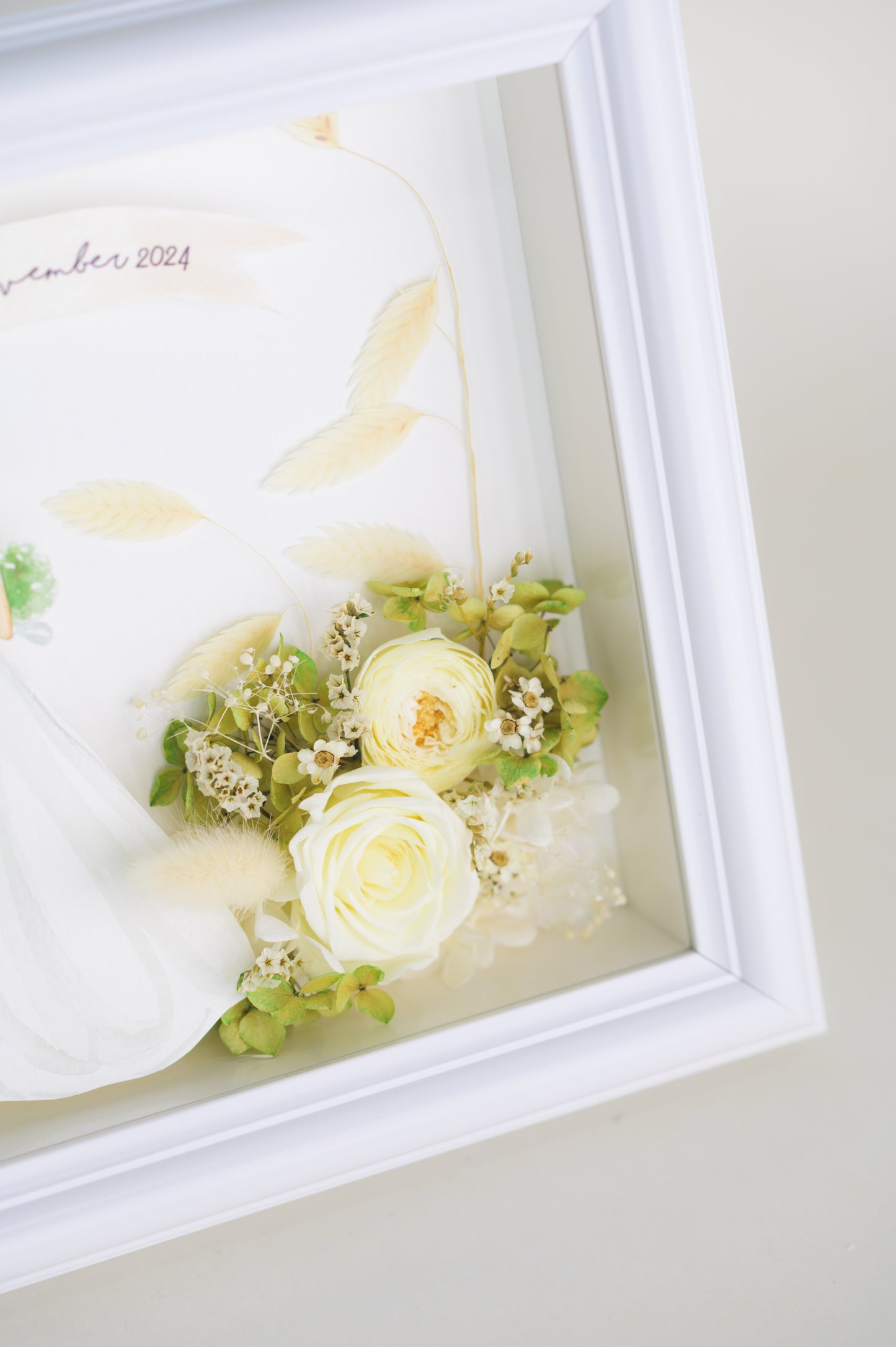 Personalized wedding frame featuring a bride and groom illustration with preserved white and green flowers, custom names and date, framed in white.