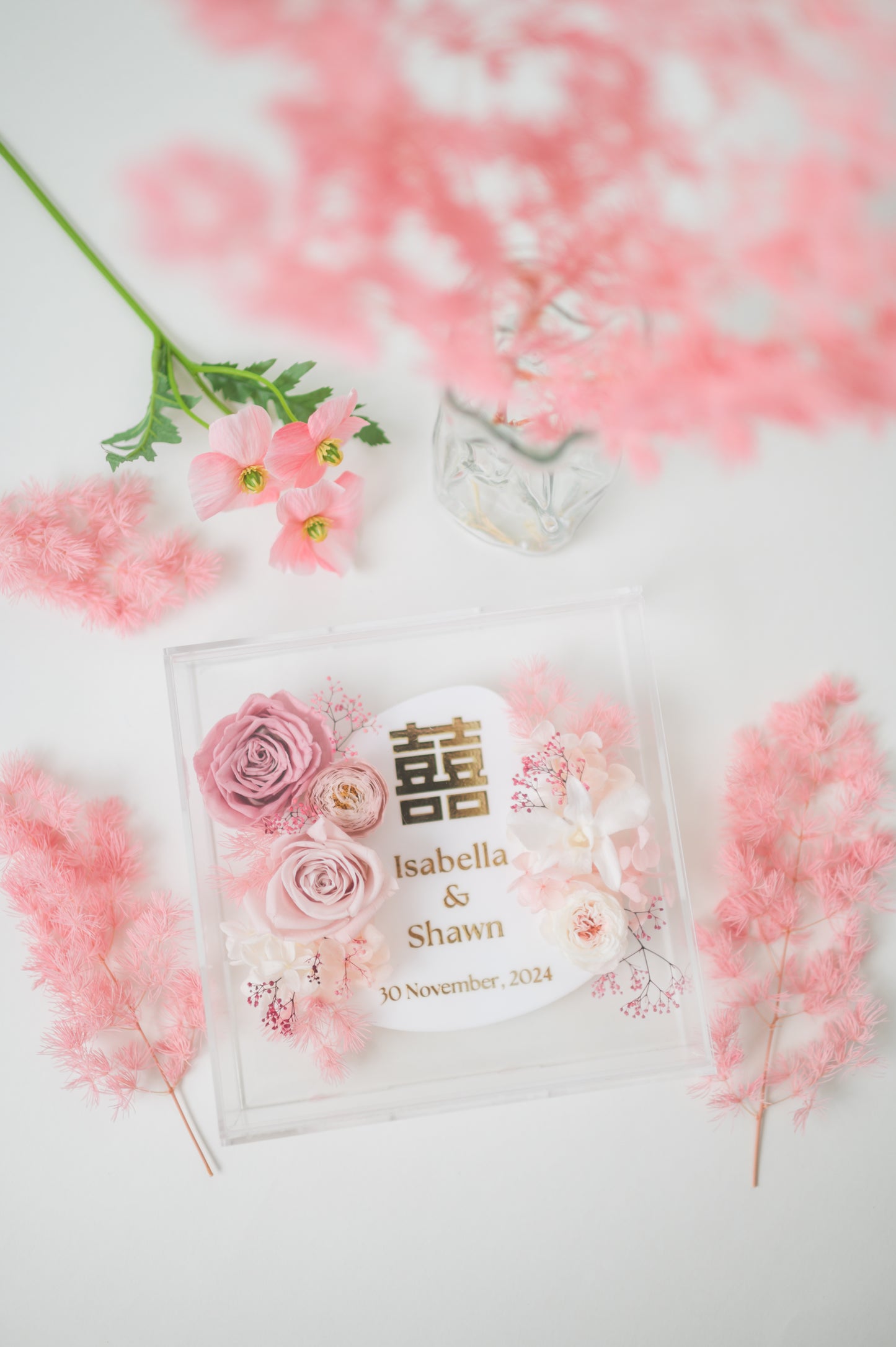 Personalized wedding frame with preserved pink flowers, featuring custom names Isabella & Shawn and a wedding date, with elegant floral design in a clear acrylic display.