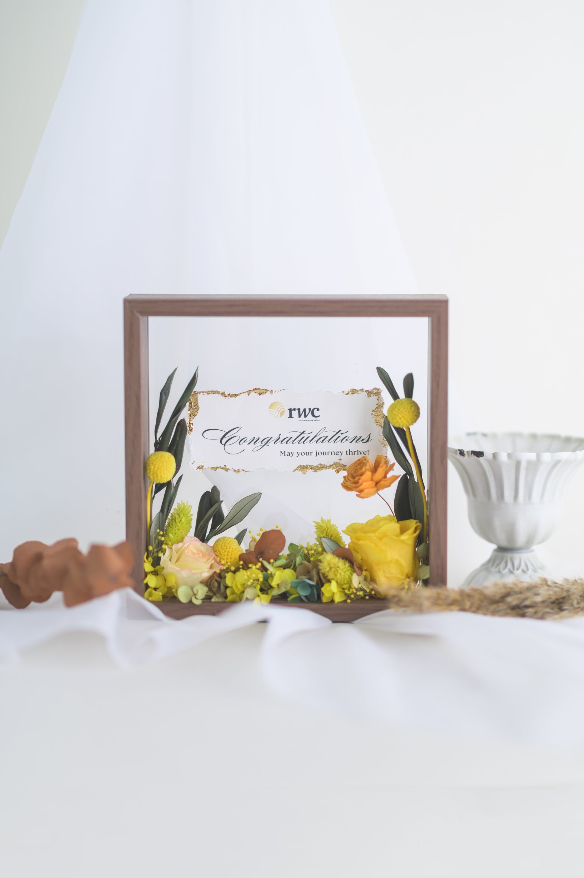 Elegant preserved flower frame with a congratulatory message, adorned with a yellow ribbon and vibrant floral arrangement, designed for a special occasion.