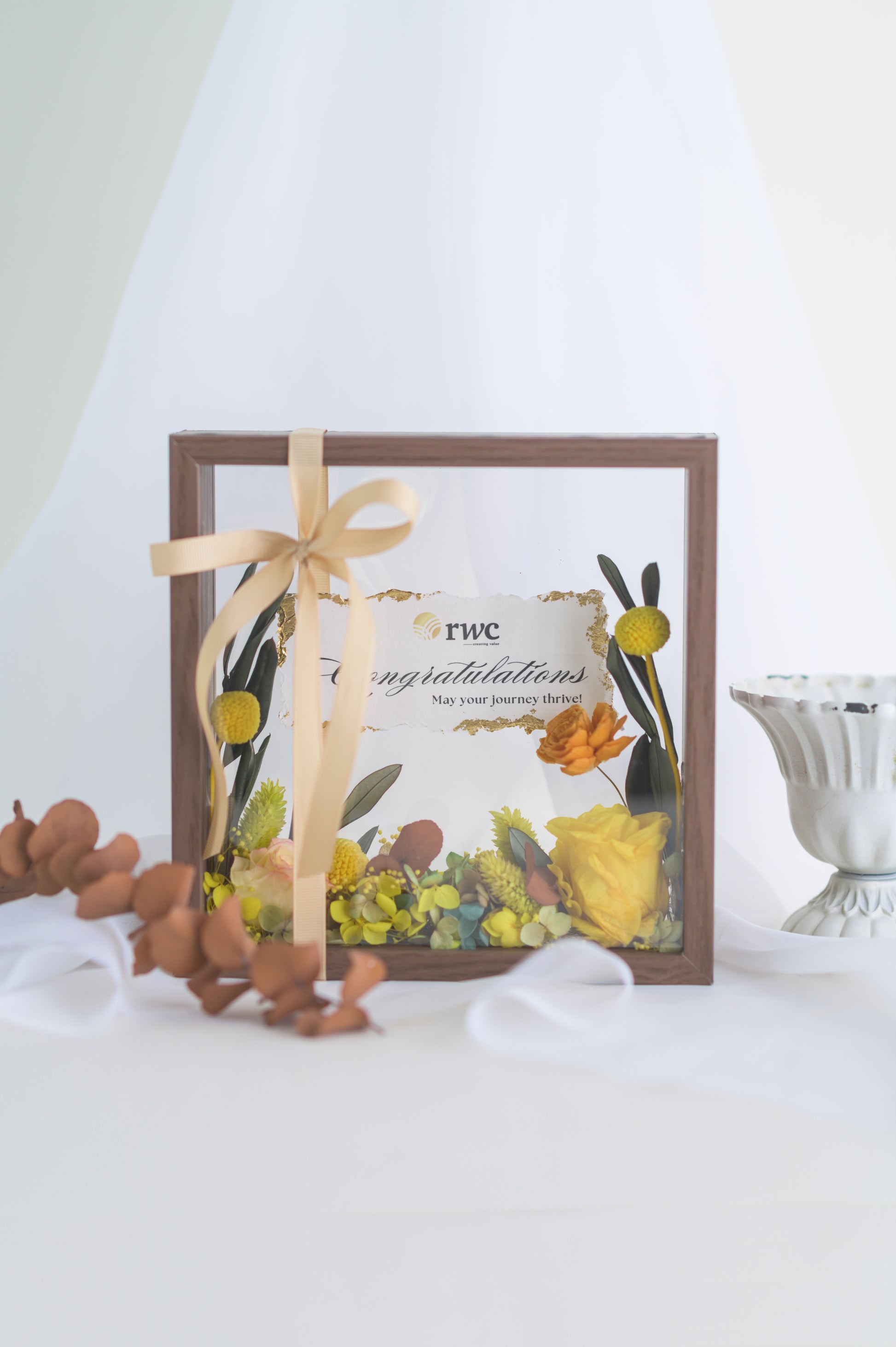 Elegant preserved flower frame with a congratulatory message, adorned with a yellow ribbon and vibrant floral arrangement, designed for a special occasion.