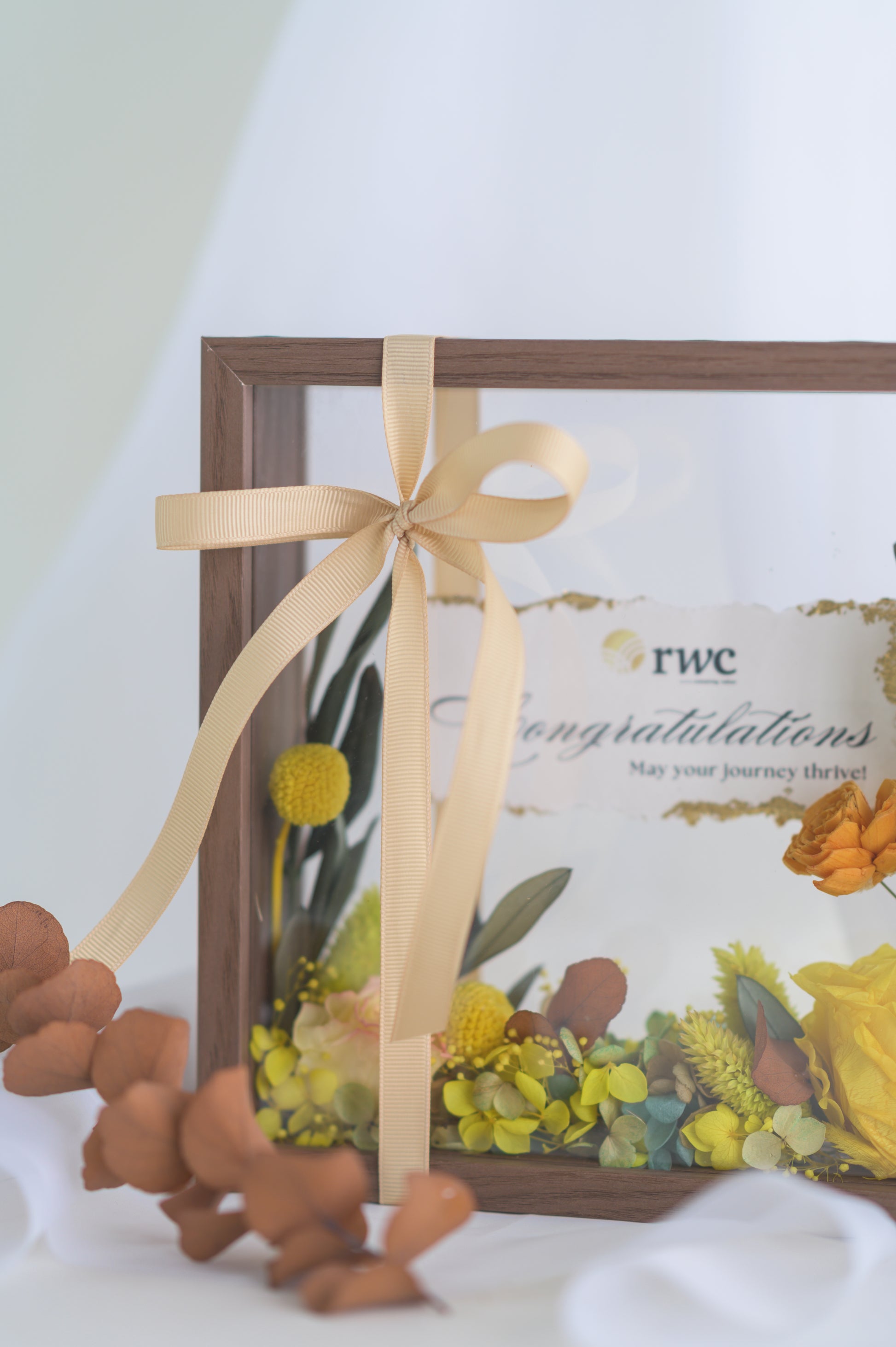 Elegant preserved flower frame with a congratulatory message, adorned with a yellow ribbon and vibrant floral arrangement, designed for a special occasion.