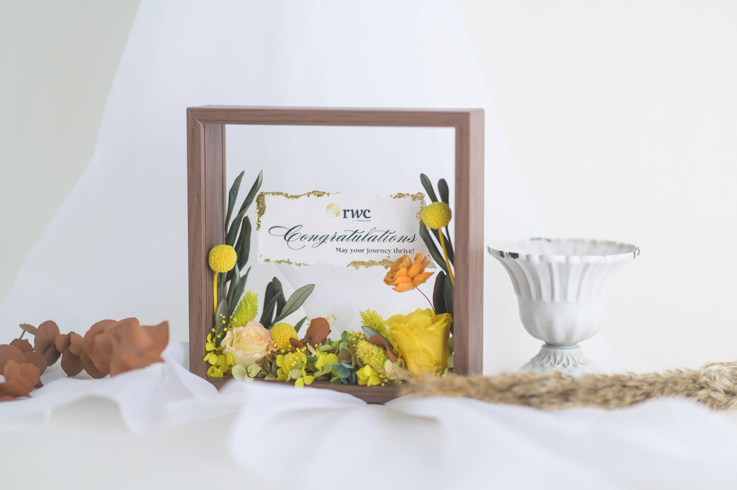 Elegant preserved flower frame with a congratulatory message, adorned with a yellow ribbon and vibrant floral arrangement, designed for a special occasion.