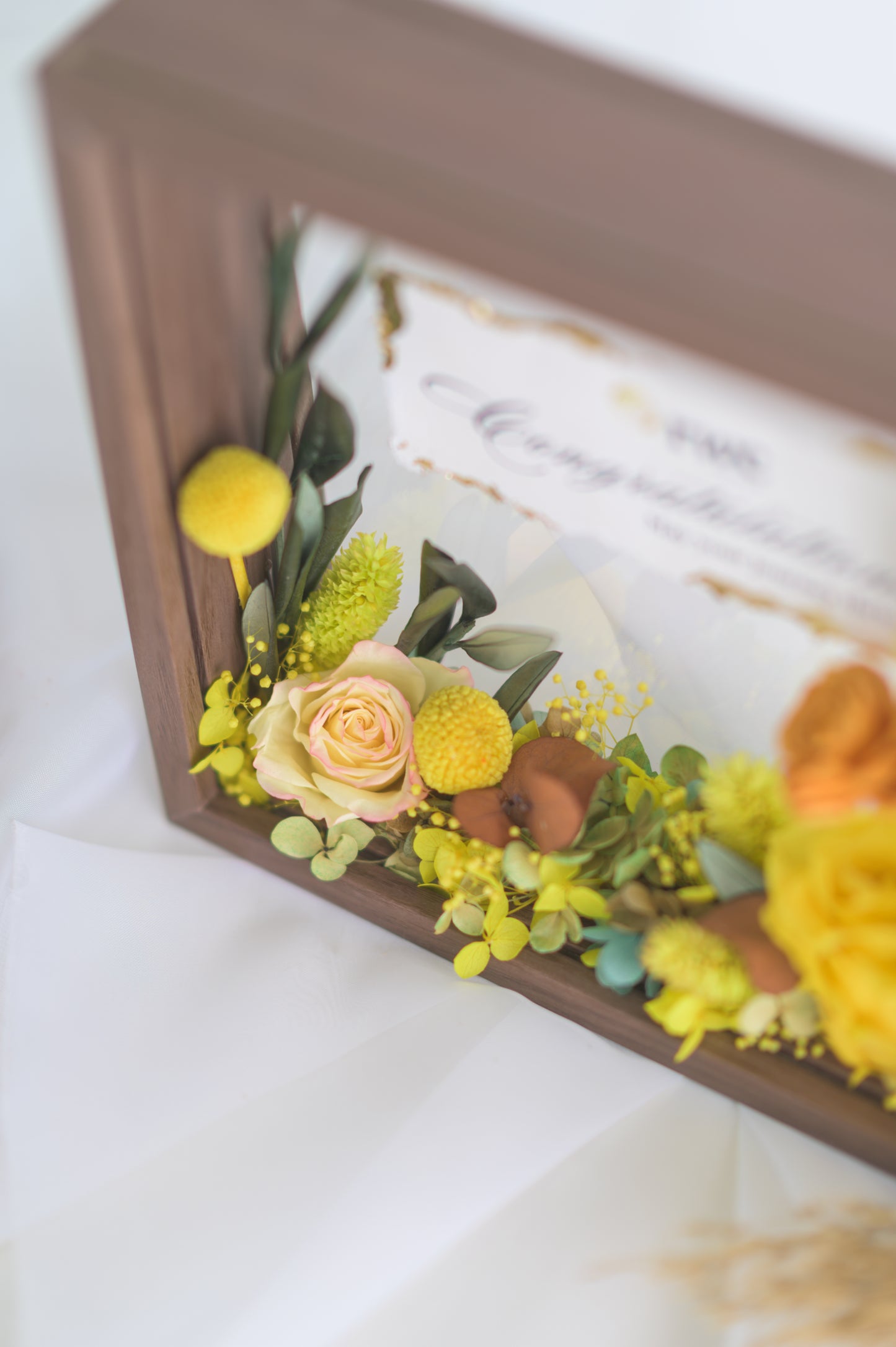 Elegant preserved flower frame with a congratulatory message, adorned with a yellow ribbon and vibrant floral arrangement, designed for a special occasion.