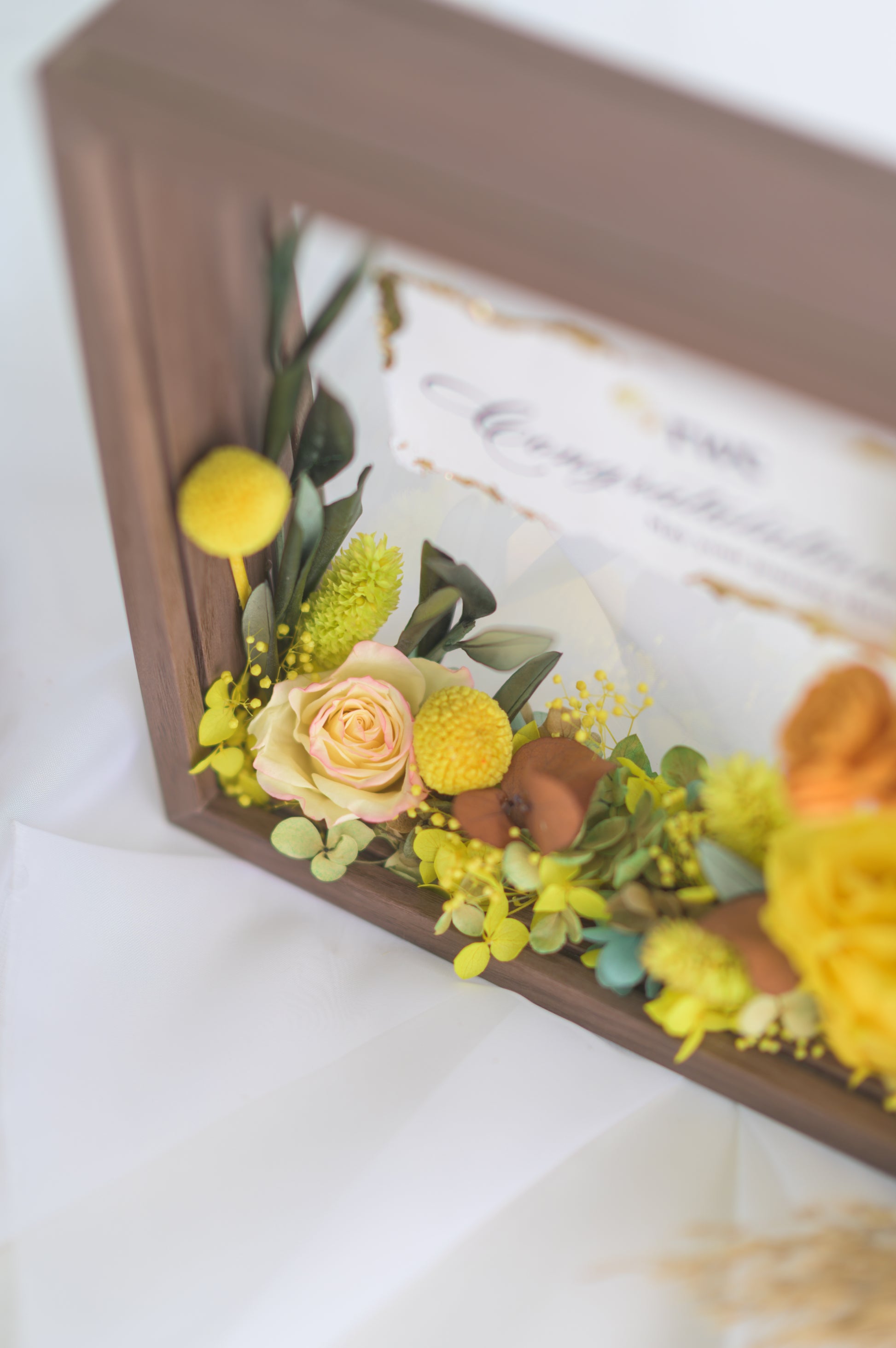 Elegant preserved flower frame with a congratulatory message, adorned with a yellow ribbon and vibrant floral arrangement, designed for a special occasion.
