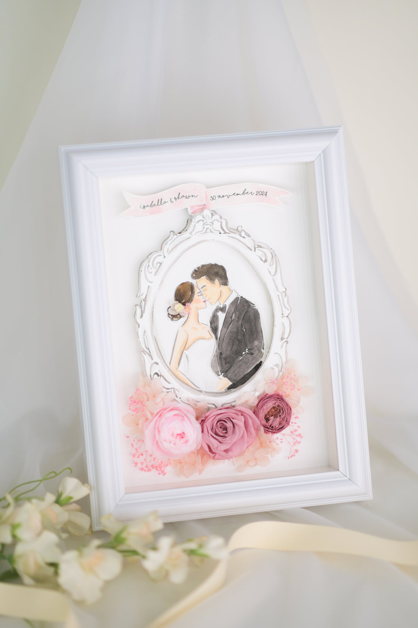 A beautifully crafted wedding frame featuring a romantic illustration of a bride and groom encased in an ornate white frame, surrounded by preserved pink roses and floral accents, personalized with names and a wedding date.