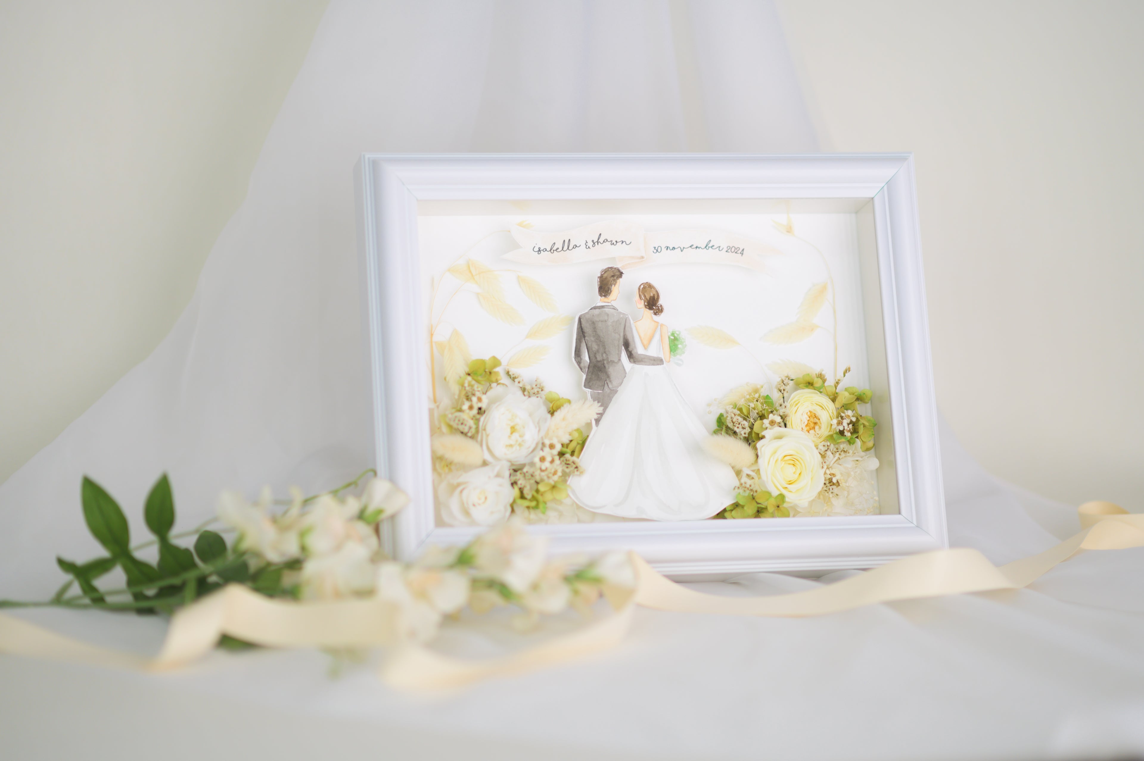 Personalized wedding frame featuring a bride and groom illustration with preserved white and green flowers, custom names and date, framed in white.