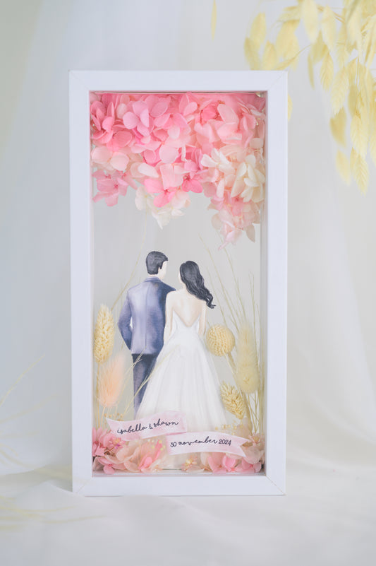A custom wedding keepsake frame featuring a couple illustration in wedding attire, surrounded by preserved flowers in soft pinks and yellows. The frame has a front and back view, offering a beautiful display of the artwork. Customizable with names and date for a personal touch.