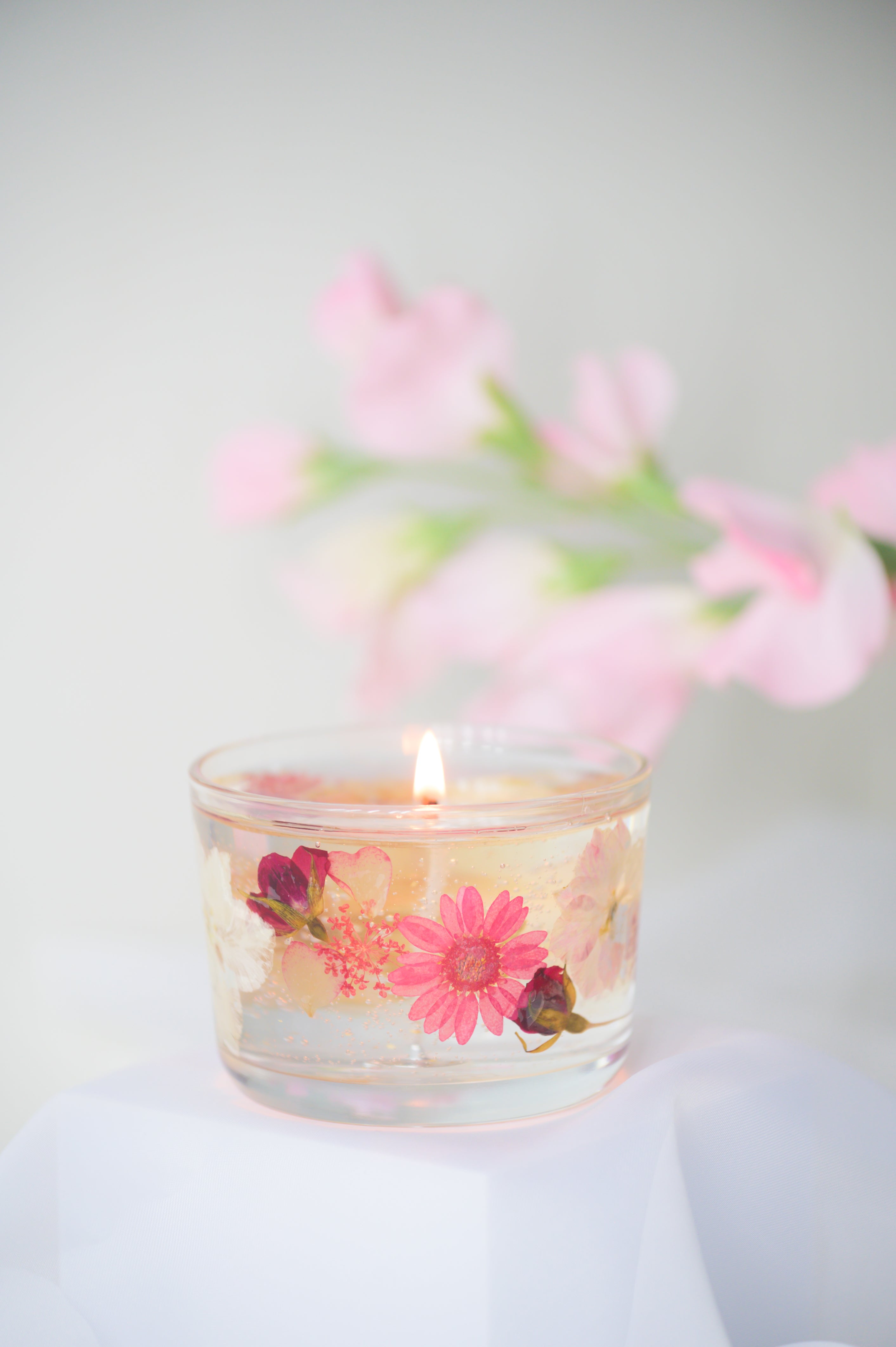 A beautiful gel candle embedded with dried pink flowers, including daisies and roses, delicately burning with soft light, creating a romantic and elegant ambiance.